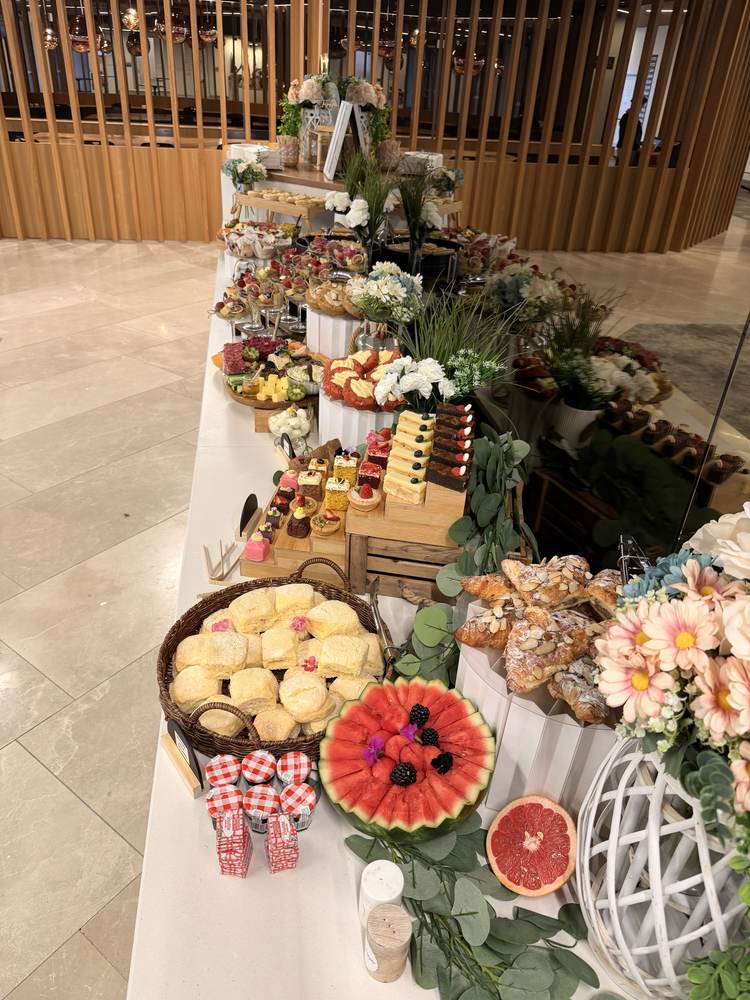 Long function grazing display with cakes, fruit platters and white flowers in a modern venue