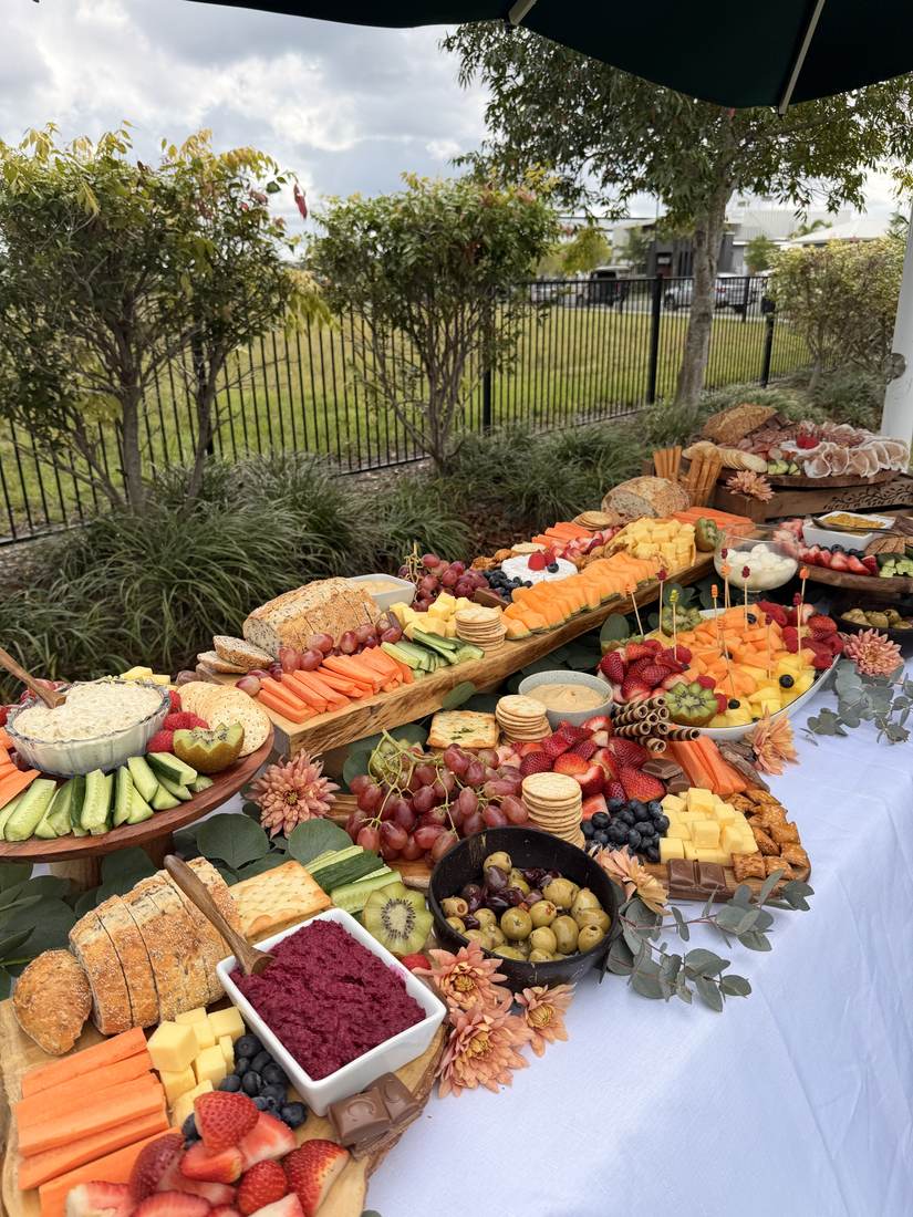 Long outdoor grazing table on a white tablecloth beside a garden